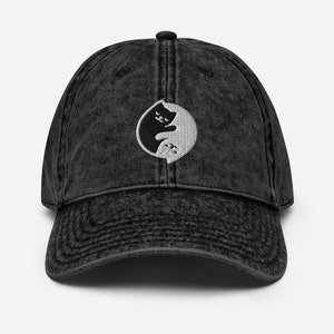 May include: A black vintage washed denim baseball cap with a white yin yang symbol featuring two cats facing each other.