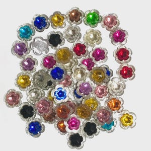 May include: Assortment of colourful flower-shaped embellishments with silver trim. The embellishments are made of plastic and have a shiny finish. They are perfect for adding a touch of sparkle to crafts, clothing, and home decor.