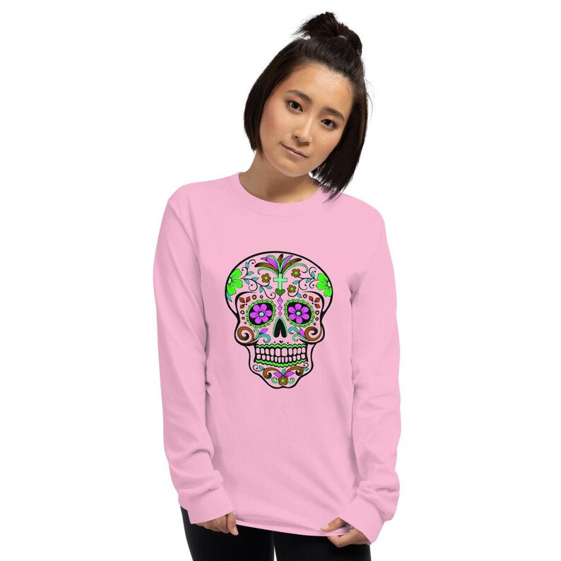 May include: A pink long-sleeved shirt with a colorful sugar skull design. The skull has green, purple, and brown details.