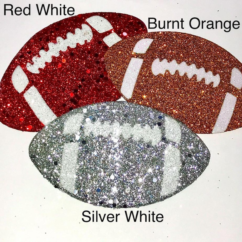 Pu&ograve; includere: Tre forme di pallone da football americano glitterate in rosso, arancione bruciato e argento. Ogni pallone ha dettagli bianchi e il testo "Red White", "Burnt Orange" e "Silver White".