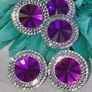 Può includere: Quattro strass viola con montature argentate. Ogni strass ha un design sfaccettato ed è circondato da un anello di strass più piccoli.
