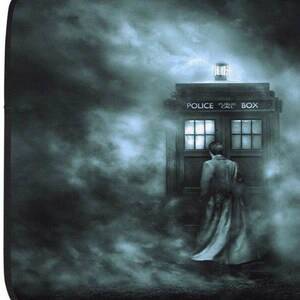 May include: A digitally created image featuring a blue police box with the words "POLICE PUBLIC CALL BOX" on top. A person in a long coat stands before the box, surrounded by a misty, atmospheric background.