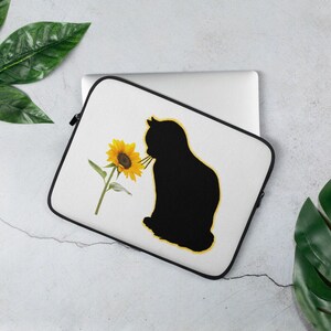 May include: A white laptop sleeve with a black silhouette of a cat smelling a yellow sunflower.