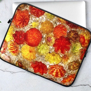 May include: A laptop sleeve with a colorful abstract design featuring red, orange, yellow, and gold glass orbs. The orbs are arranged in a random pattern and appear to be floating in a clear liquid.