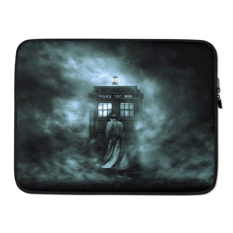 May include: Black laptop sleeve featuring a scene with a blue police box and a person in a long coat. The police box has the words "POLICE BOX" on top. The background is a dark, misty scene.