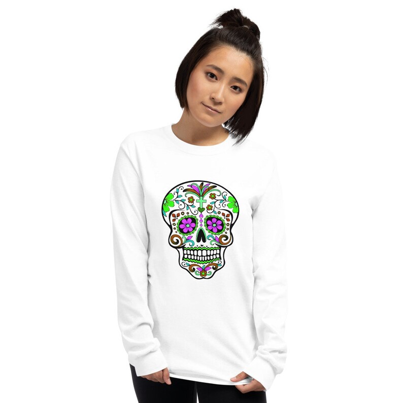 May include: White long-sleeve shirt with a colorful sugar skull design. The skull has green, pink, and brown details.