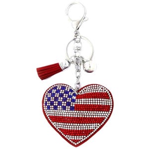 May include: A red heart-shaped keyring with a sparkly American flag design. The keyring has a silver chain with a tassel and a bell charm.