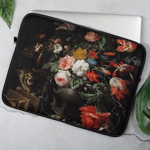 Op de afbeelding: Een laptophuls met een vintage stillevenschilderij van een vaas vol kleurrijke bloemen, waaronder rode tulpen, roze rozen en witte bloesems. Een kat met groene ogen zit op een houten kist op de voorgrond.