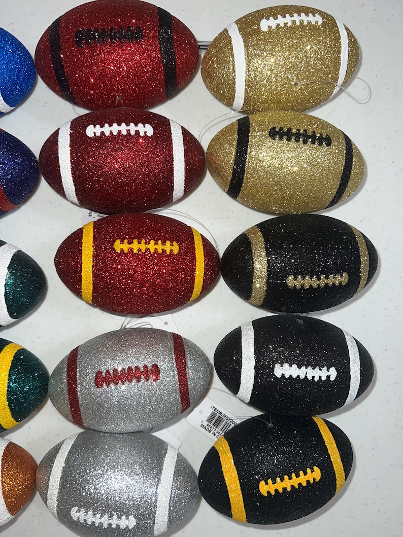 May include: Glitter-covered football ornaments in various colors, including red, gold, black, and silver. Each ornament features white or yellow stripes and laces, perfect for holiday decorations or sports-themed crafts.