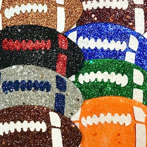Pu&ograve; includere: Una collezione di ornamenti a forma di pallone da football americano glitterati in vari colori, tra cui oro, marrone, nero, argento, blu, verde e arancione. Ogni ornamento presenta cuciture e marcature bianche, perfetto per lavori creativi o decorazioni a tema sportivo.