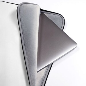 May include: A gray laptop sleeve with a black zipper and a soft gray lining. A silver laptop is partially inside the sleeve.