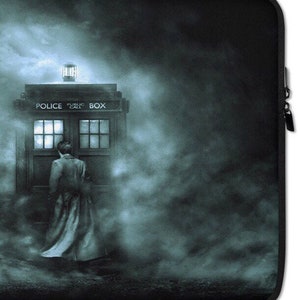 May include: A black laptop sleeve featuring a blue-toned image of a police box with the words "POLICE PUBLIC CALL BOX" on top. A person in a long coat stands near the box, surrounded by a misty atmosphere.