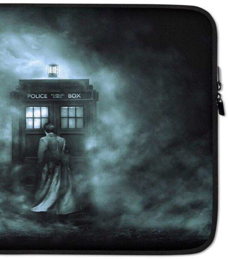 May include: A black laptop sleeve featuring a blue-toned image of a police box with the words "POLICE PUBLIC CALL BOX" on top. A person in a long coat stands near the box, surrounded by a misty atmosphere.