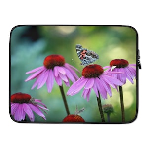 Puede incluir: Una mariposa con alas negras, blancas y rojas se posa sobre una flor rosa con un centro rojo. La flor está rodeada de otras flores rosas con centros rojos. El fondo es un verde borroso.