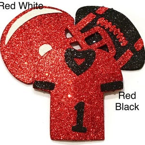 Pu&ograve; includere: Decorazione glitterata a tema football americano con casco, maglia con il numero 1 e pallone da football. Il casco ha dettagli bianchi, mentre la maglia e il pallone hanno dettagli neri. Sono visibili le parole "Red White" e "Red Black".