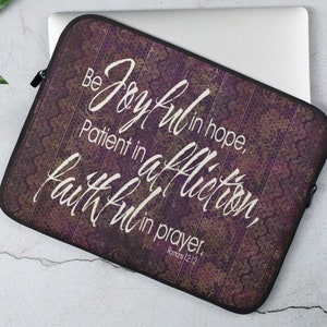 Puede incluir: Funda para portátil de color morado con una cita de Romanos 12:12, "Estad alegres en la esperanza, pacientes en la tribulación, constantes en la oración."