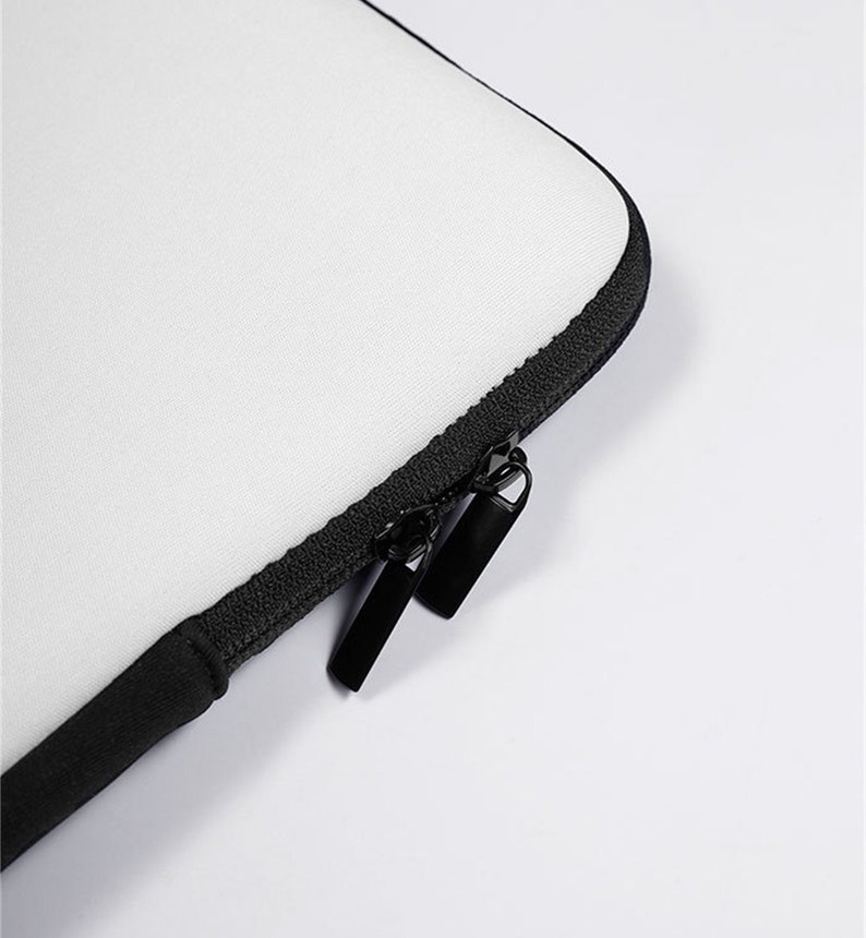 May include: A white laptop sleeve with a black zipper and trim. The sleeve is made of a soft, textured material. The zipper has two black pulls.