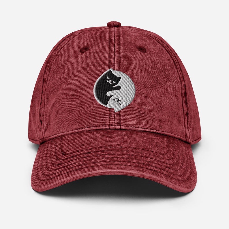 May include: A red vintage washed cotton baseball cap with an embroidered yin yang symbol featuring two black cats facing each other.