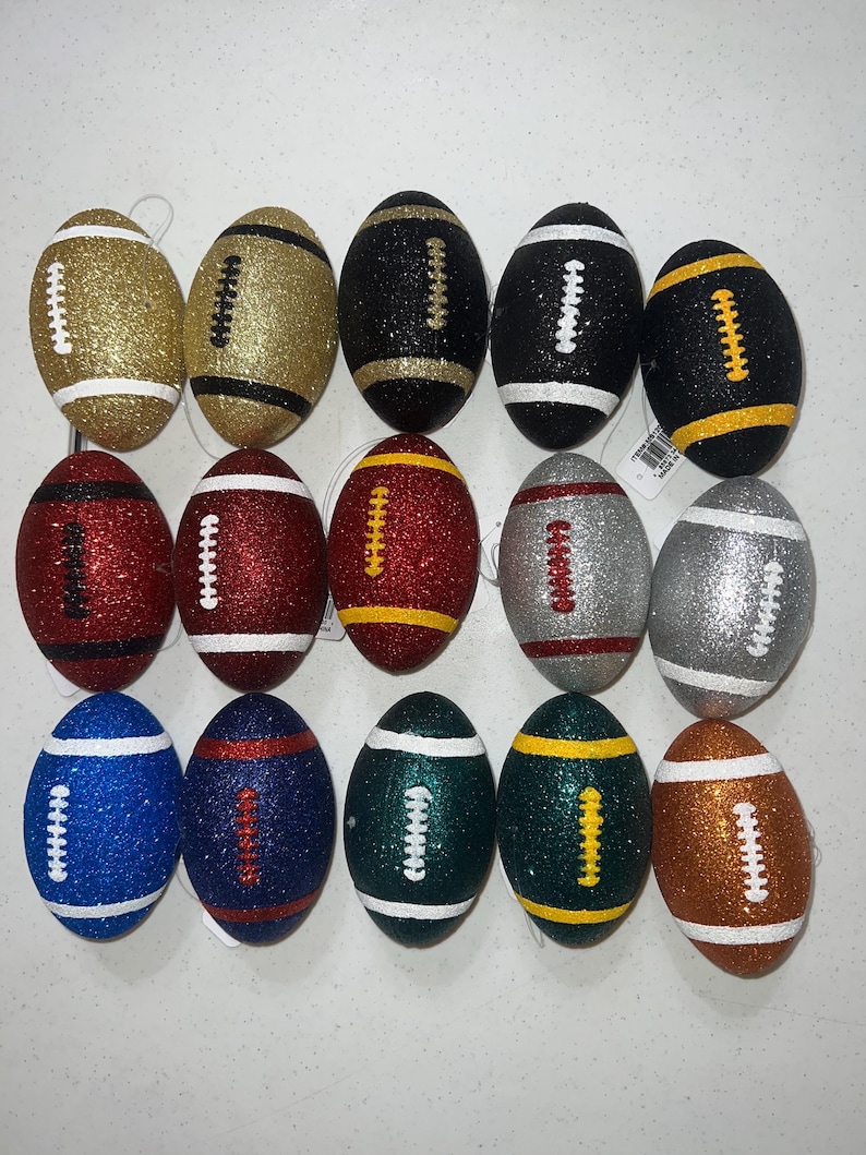 May include: A collection of fifteen glitter-covered football ornaments in various colors. The ornaments include gold, black, red, silver, blue, green, and brown, each with white or yellow stitching details. These decorative footballs are ideal for sports-themed decor.