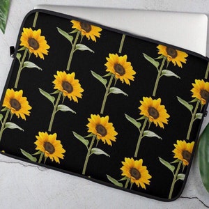 Puede incluir: Funda para portátil negra con un patrón repetido de girasoles amarillos sobre un fondo negro.