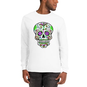 May include: White long-sleeve t-shirt with a colorful sugar skull design. The skull has green, pink, and brown details.
