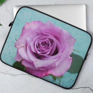 Puede incluir: Una rosa púrpura con gotas de agua en los pétalos, sobre un fondo azul claro. La rosa está enfocada, y el fondo está desenfocado.