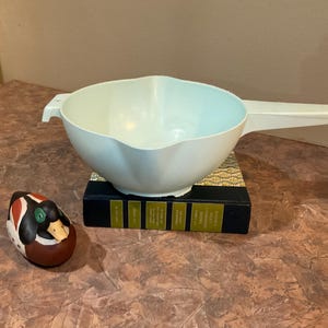 May include: A light blue plastic colander with a handle. The colander is sitting on top of a book.