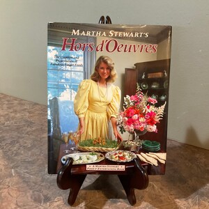 May include: A cookbook titled "Martha Stewart's Hors d'Oeuvres: The Creation and Presentation of Fabulous Finger Foods" with a photo of Martha Stewart on the cover. The cover features a yellow dress, a floral arrangement, and a table setting with food.