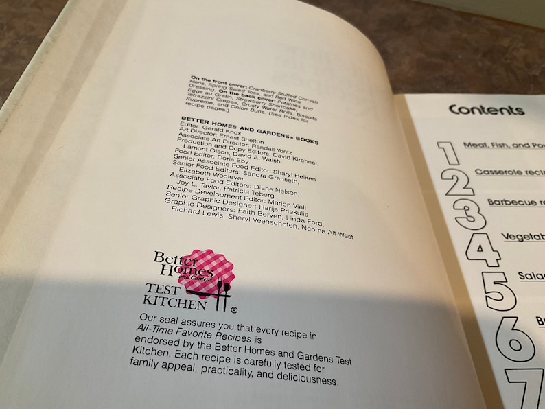 May include: A white book with a red and white gingham pattern on the cover. The book title is "Better Homes and Gardens Test Kitchen". The book cover also includes the text "Our seal assures you that every recipe in All-Time Favorite Recipes is endorsed by the Better Homes and Gardens Test Kitchen. Each recipe is carefully tested for family appeal, practicality, and deliciousness."
