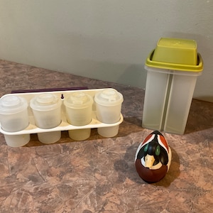 Könnte beinhalten: Ein Satz mit vier durchsichtigen Plastikbehältern mit Deckeln, ein durchsichtiger Plastikbehälter mit grünem Deckel und eine bemalte Holz-Entenfigur.