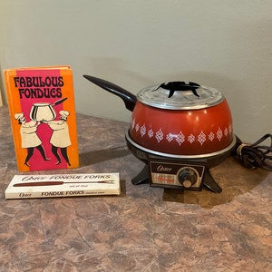 May include: Vintage Oster fondue set with a red and white pot, a black base, and a control knob. The set includes a cookbook titled "Fabulous Fondues" and a box of fondue forks.
