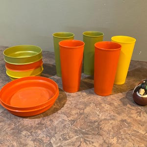Könnte beinhalten: Ein Set aus sechs Vintage-Plastikbechern in den Farben Gelb, Orange und Grün. Die Becher stehen auf einer braunen Oberfläche. Außerdem gibt es eine kleine orange Schüssel und eine hölzerne Entenattrappe.