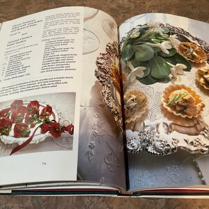 May include: An open cookbook with two pages showing recipes for Cherry Tomatoes Filled with Artichoke and Hearts of Palm and Oriental Chicken Salad Tartlets. The left page shows a silver platter with red and green tartlets. The right page shows a silver platter with white flowers and four small tartlets filled with a green and white mixture.