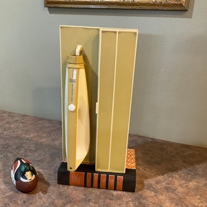 May include: A vintage Sunbeam electric knife in its original box. The knife is beige and white with a chrome button. The box is beige with a brown trim.