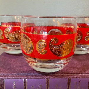 May include: Set of three red and gold glass tumblers with a paisley pattern. The glasses are clear and have a wide base.