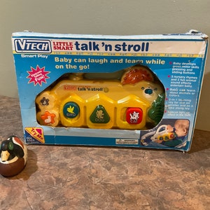 May include: A yellow and green VTech Little Smart talk 'n stroll toy for babies. The toy has buttons with pictures of a bird, dog, and cat. The box says "Baby can laugh and learn while on the go!" and "Try Me".
