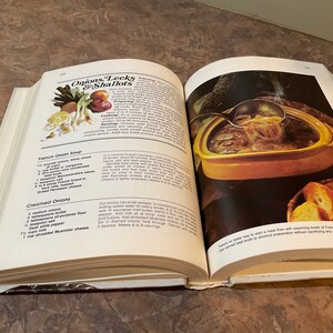 May include: Open cookbook with a recipe for French Onion Soup. The recipe includes ingredients like onions, thyme, butter, beef broth, and Gruyere cheese. The image shows a bowl of French Onion Soup with a ladle scooping out some of the soup. There are also some slices of bread on a plate next to the bowl.