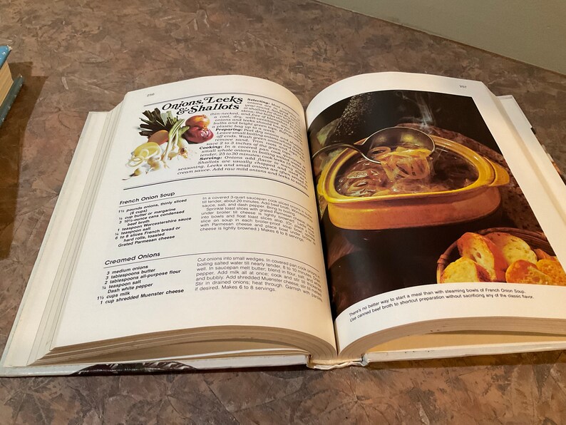 May include: Open cookbook with a recipe for French Onion Soup. The recipe includes ingredients like onions, thyme, butter, beef broth, and Gruyere cheese. The image shows a bowl of French Onion Soup with a ladle scooping out some of the soup. There are also some slices of bread on a plate next to the bowl.