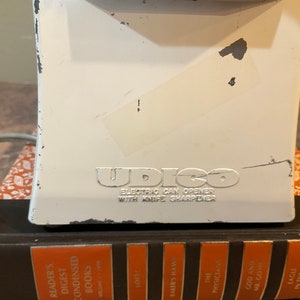 Peut inclure: Ouvre-bo&icirc;te &eacute;lectrique blanc avec un logo "UDICO" argent&eacute; et le texte "ELECTRIC CAN OPENER WITH KNIFE SHARPENER".