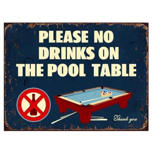 May include: A blue and red metal sign with the text "Please No Drinks On The Pool Table" and a red circle with a diagonal line through a bottle. The sign also features a pool table with balls and a cue stick.