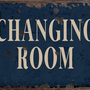 May include: A blue metal sign with white text that reads "CHANGING ROOM". The sign has a distressed, rusty look.
