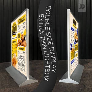 May include: Double-sided lightbox display with a silver frame and a white background. The display features a menu with a variety of food items, including fried chicken, fries, and sandwiches. The text on the menu reads "Delicious Chicken", "Fried Potato", "Sandwich", and "The Most Delicious".