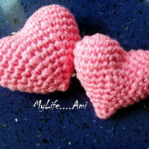 May include: Two pink crocheted hearts on a blue background. The hearts are made with a textured stitch and are a symbol of love.