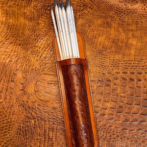May include: A brown leather pencil case with a textured ostrich-like pattern and visible stitching, containing several white pencils with black leads. The leather case features the embossed text CHAV on the front upper edge and a pointed base.