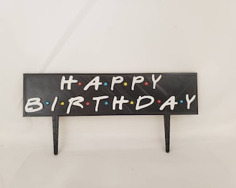 May include: Black cake topper with white letters spelling "HAPPY BIRTHDAY" in the style of the popular TV show "Friends".