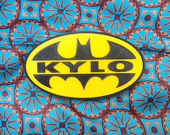 May include: A yellow and black Batman logo with the name "KYLO" written in black letters across the center.