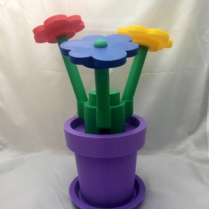May include: A purple flower pot with a green base and three colorful flowers. The flowers are red, blue, and yellow.