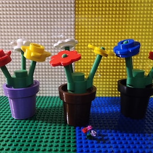 May include: Five colorful Lego flower pots with different colored flowers. The pots are on a green and blue Lego baseplate.