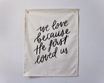 Wir lieben, weil er uns zuerst geliebt hat | Minimalistischer christlicher Wandbehang auf 100% Baumwolle | 1 Johannes 4:19 Schrift Wandkunst