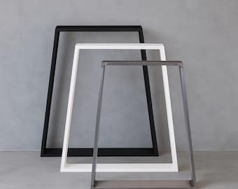 Può includere: Tre moderne cornici in metallo, nere, bianche e grigie. Le cornici hanno una forma rettangolare con un design leggermente trapezoidale, adatte per esporre opere d'arte o come elementi decorativi. Il design minimalista si adatta a vari stili di interni.